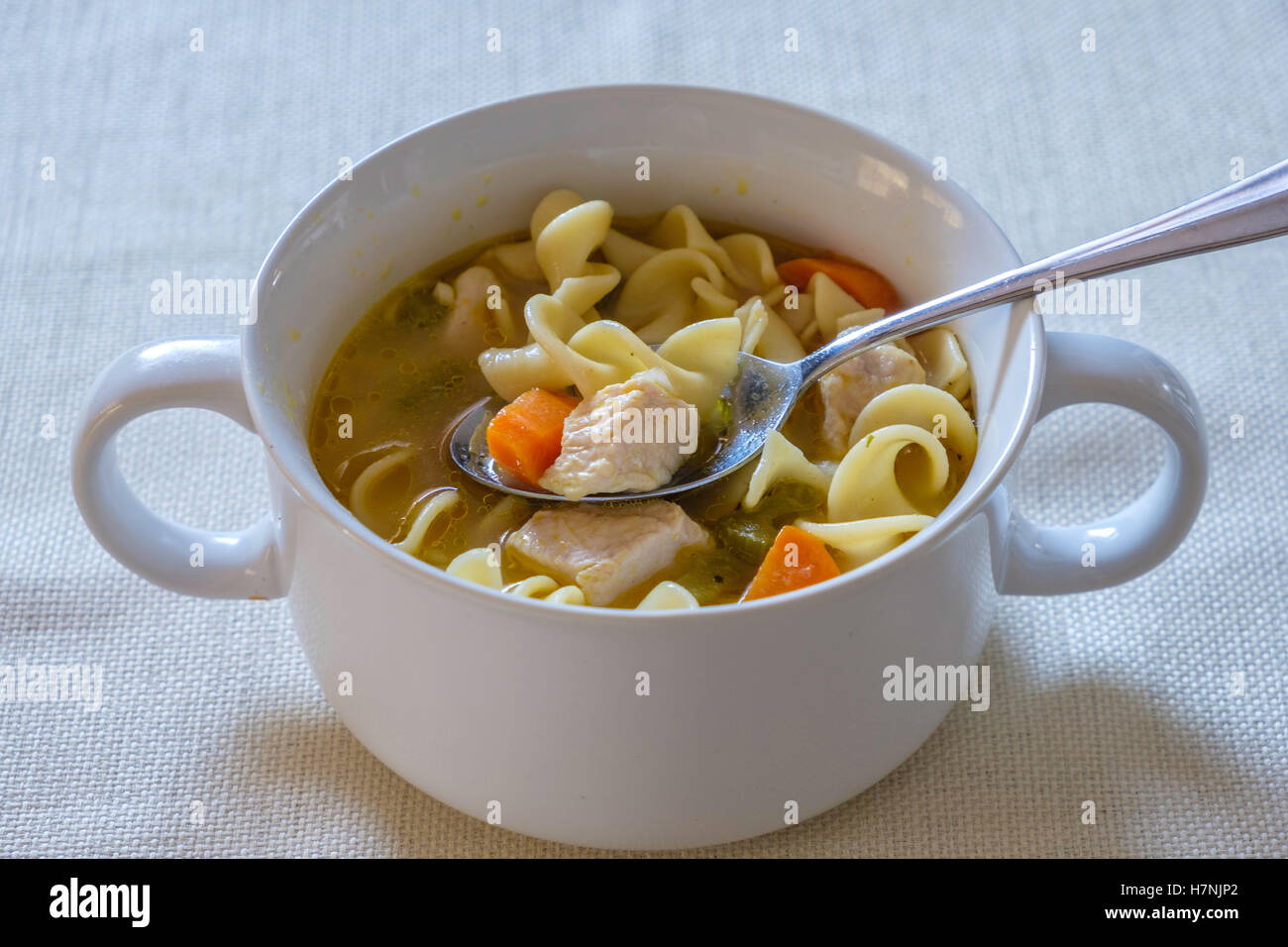 Home made chicken noodle soup, comfort food, containing carrots and celery served in a white bowl. Closeup. Stock Photo