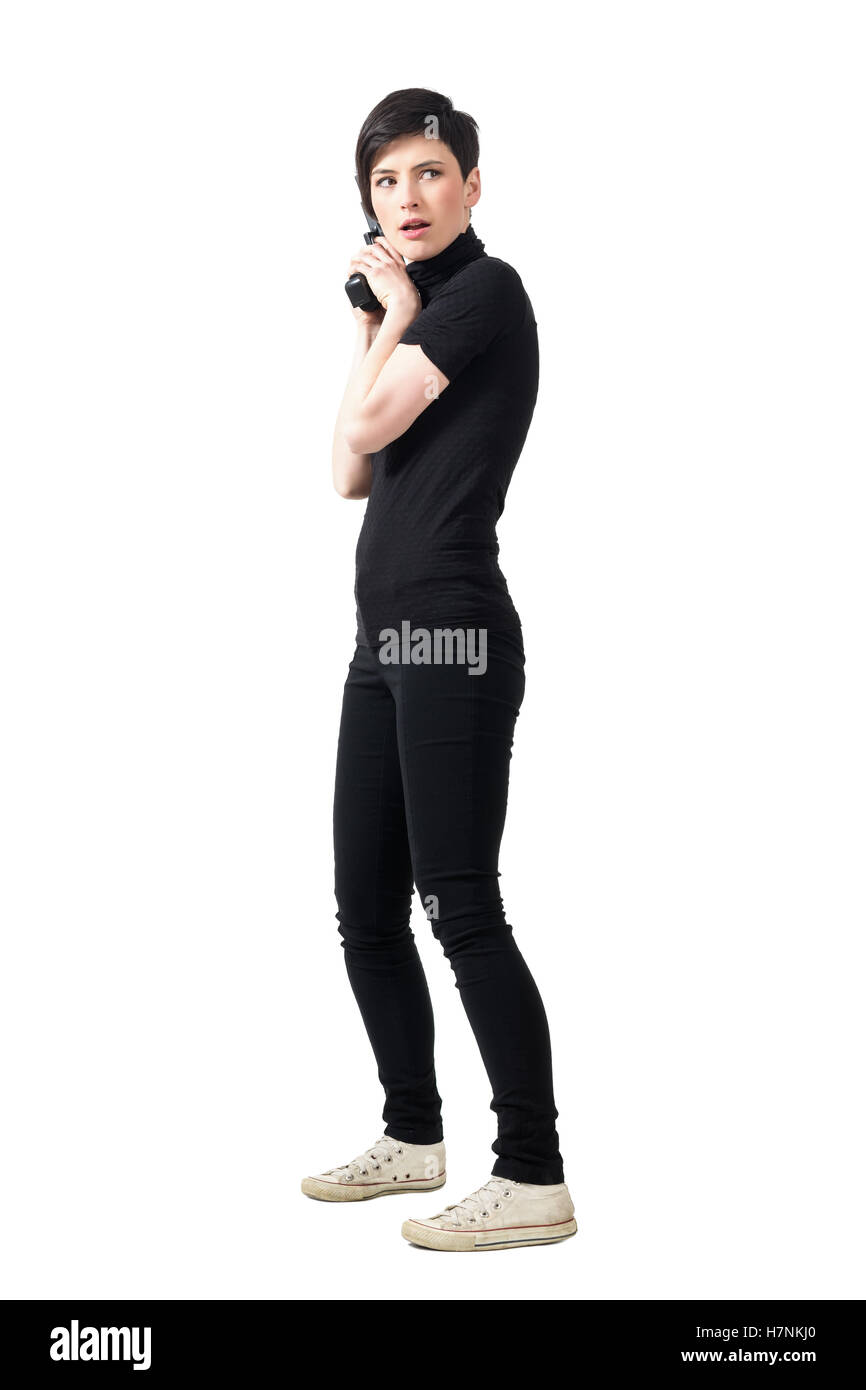 Side view of cautious female spy in black clothes with gun looking behind. Full body length portrait isolated on white Stock Photo