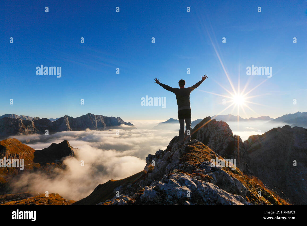 Climber on top of the mountain peak with spred hands watchiing the sun Stock Photo