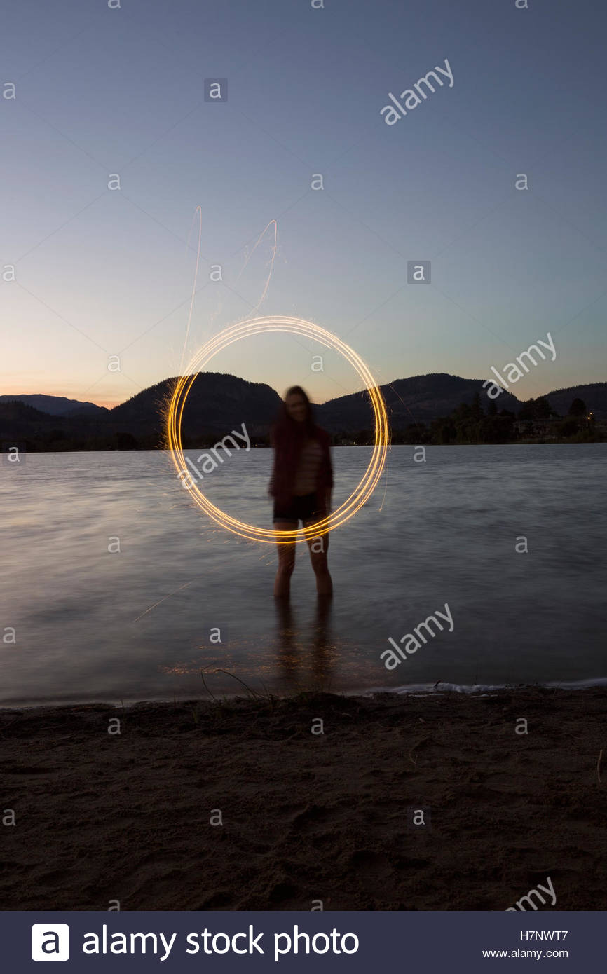 Young woman swirling fireworks in lake at dusk Stock Photo