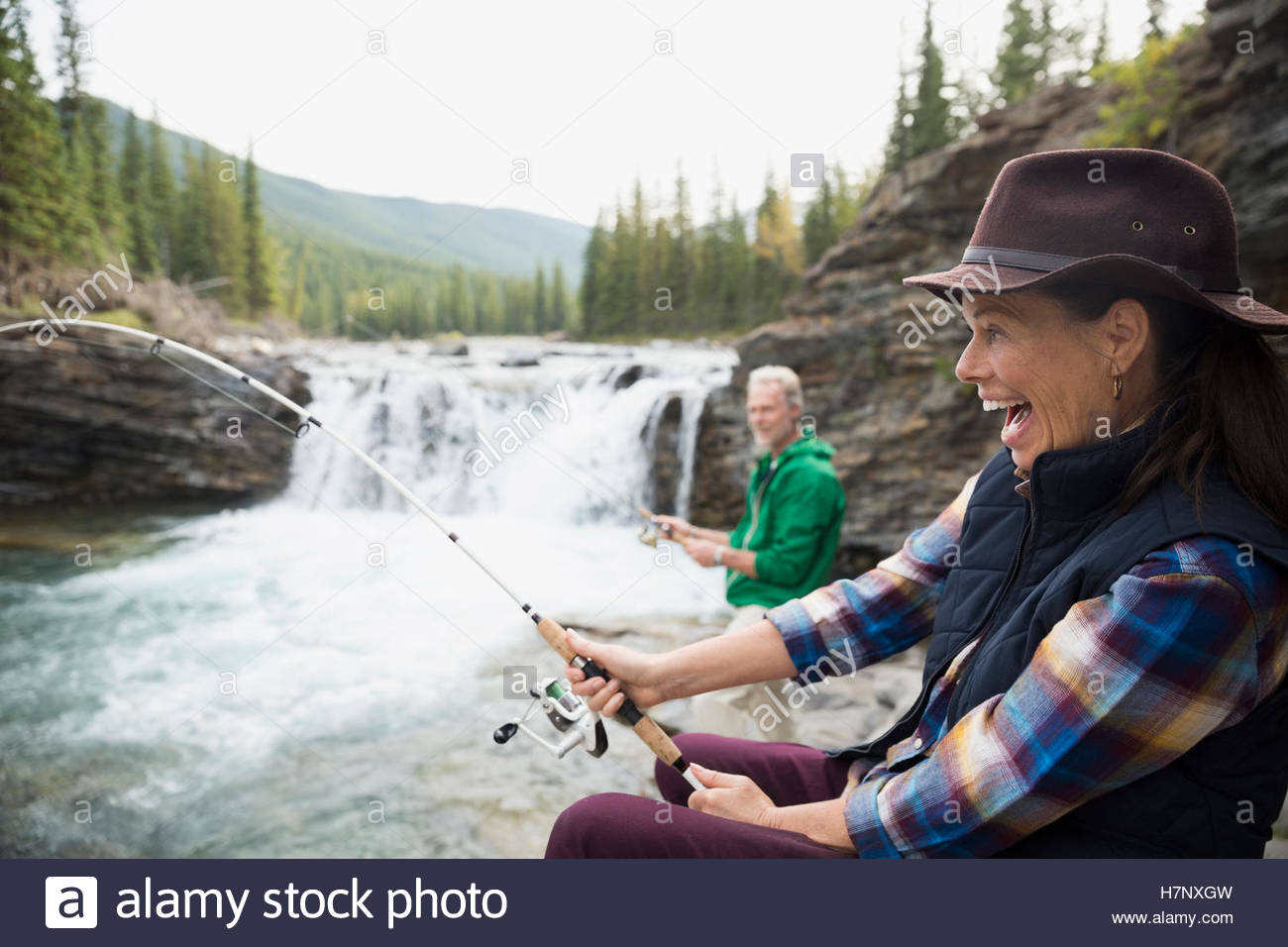 Enthusiastic senior woman fishing catching fish at waterfall Stock Photo