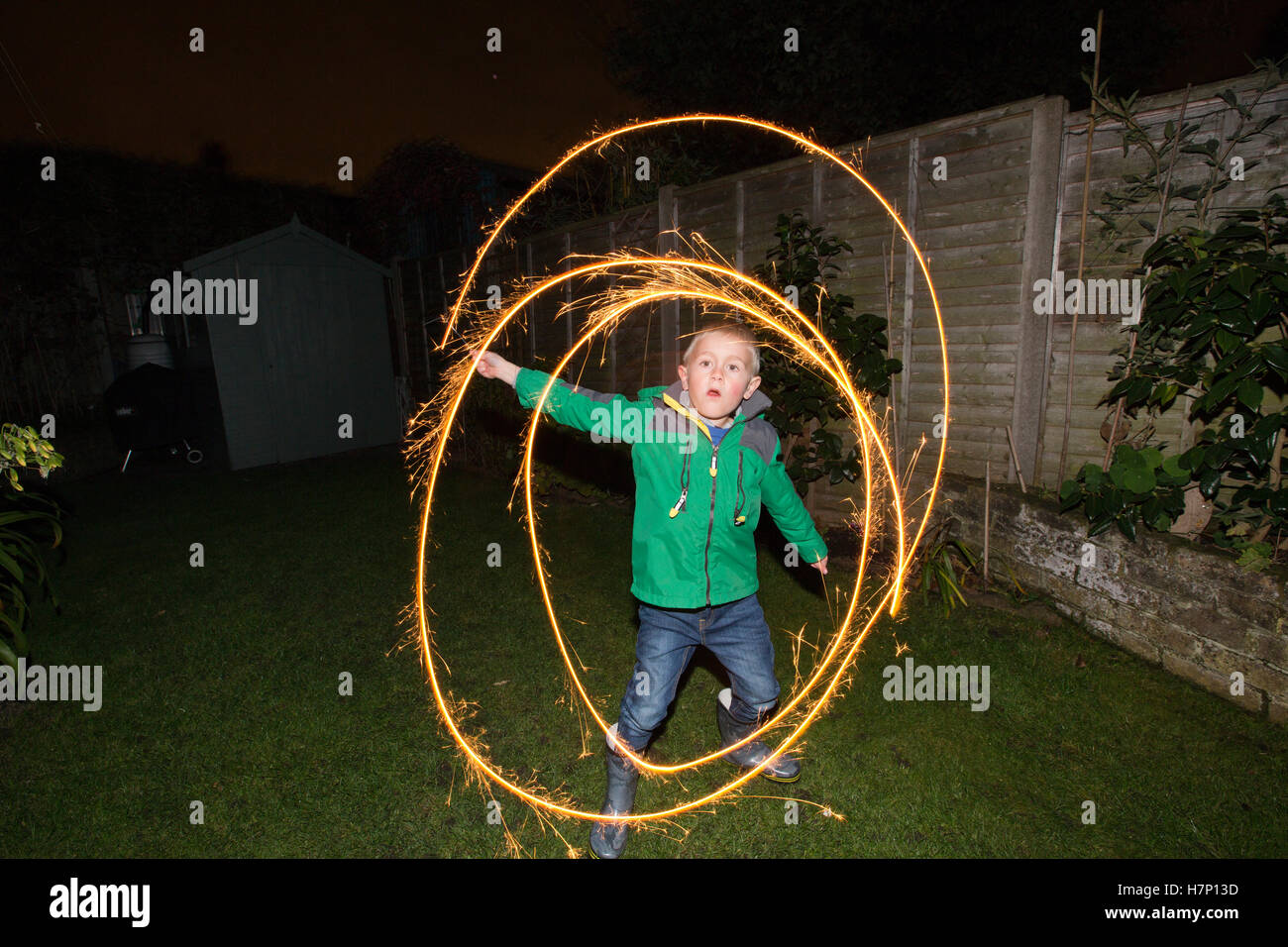 Boy (aged 5) in suburban backgarden with hand-held firework type 'sparkler' on Bonfire night or traditionally Guy Fawkes night. Stock Photo