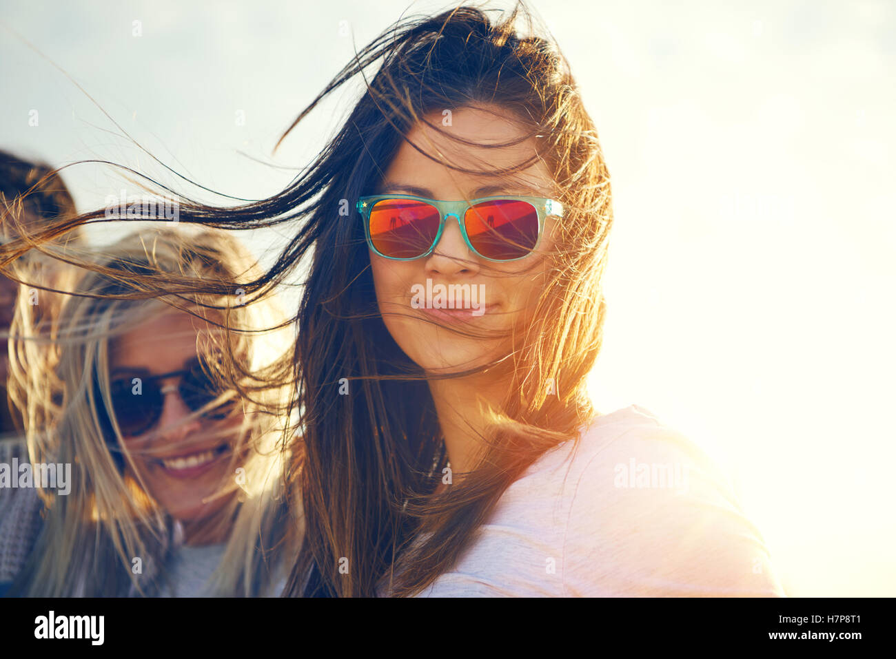 Two gorgeous trendy young women enjoying the breze on a hot summer day standing in their sunglasses smiling at the camera, close Stock Photo