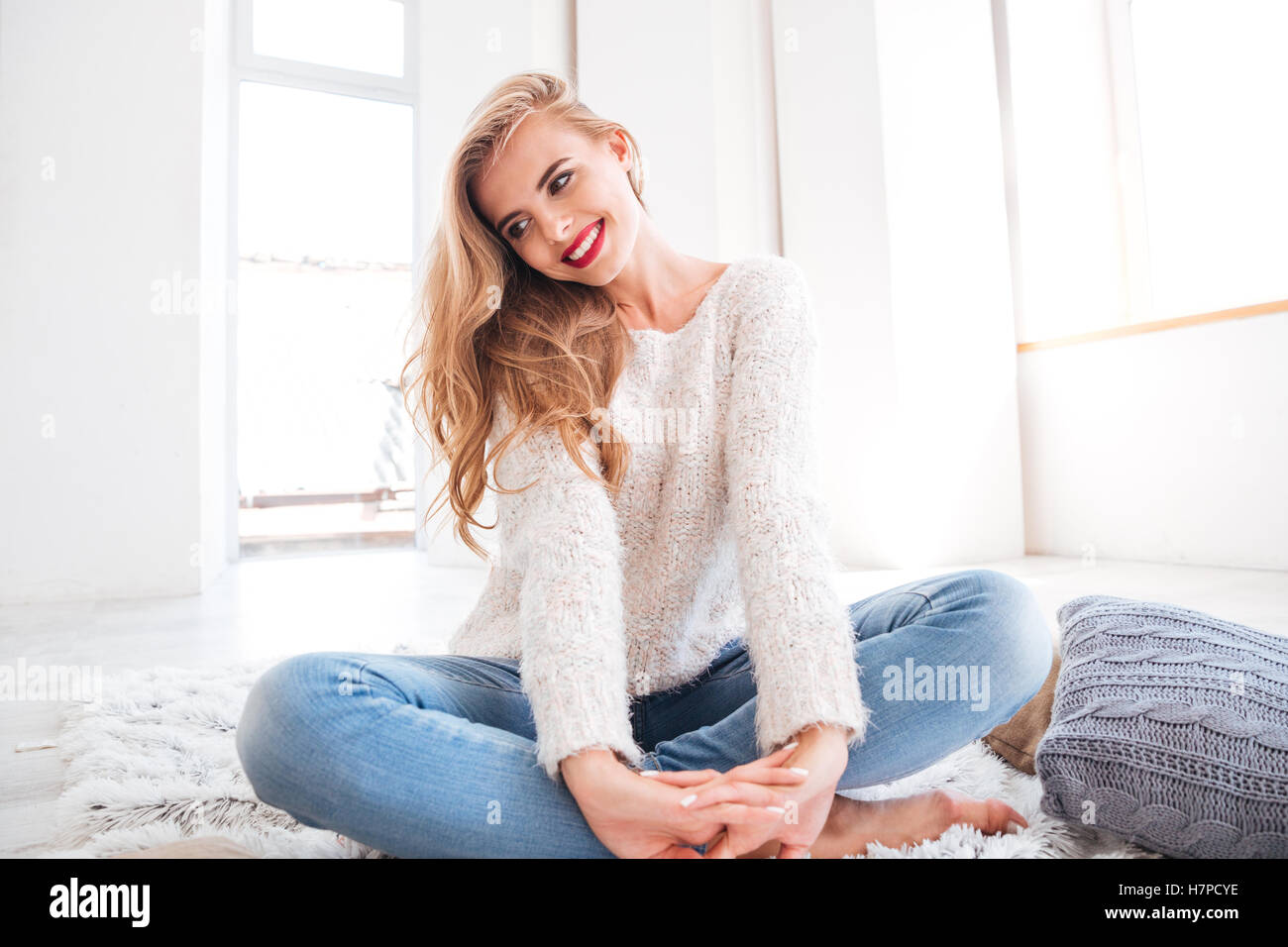 Beautiful charming woman wearing sweater and red lipstick sitting on the carpet at home Stock