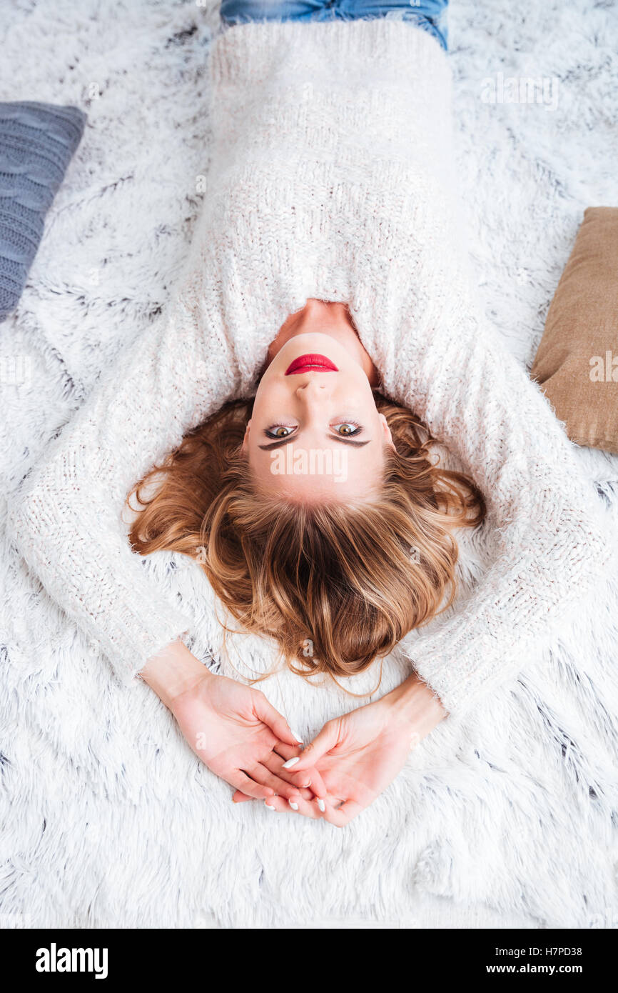 Top view of a charming pretty woman wearing red lipstick and sweater lying on the carpet Stock Photo