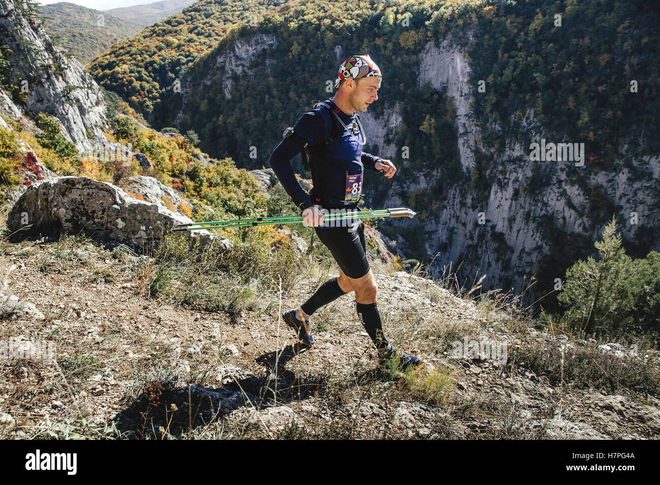 young male runner with walking poles running through steep cliff during Crimea mountain marathon Stock Photo