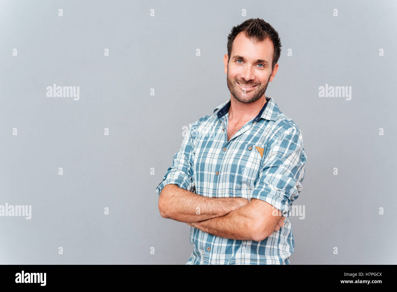 Portrait of a smiling man standing with hands crossed over gray ...