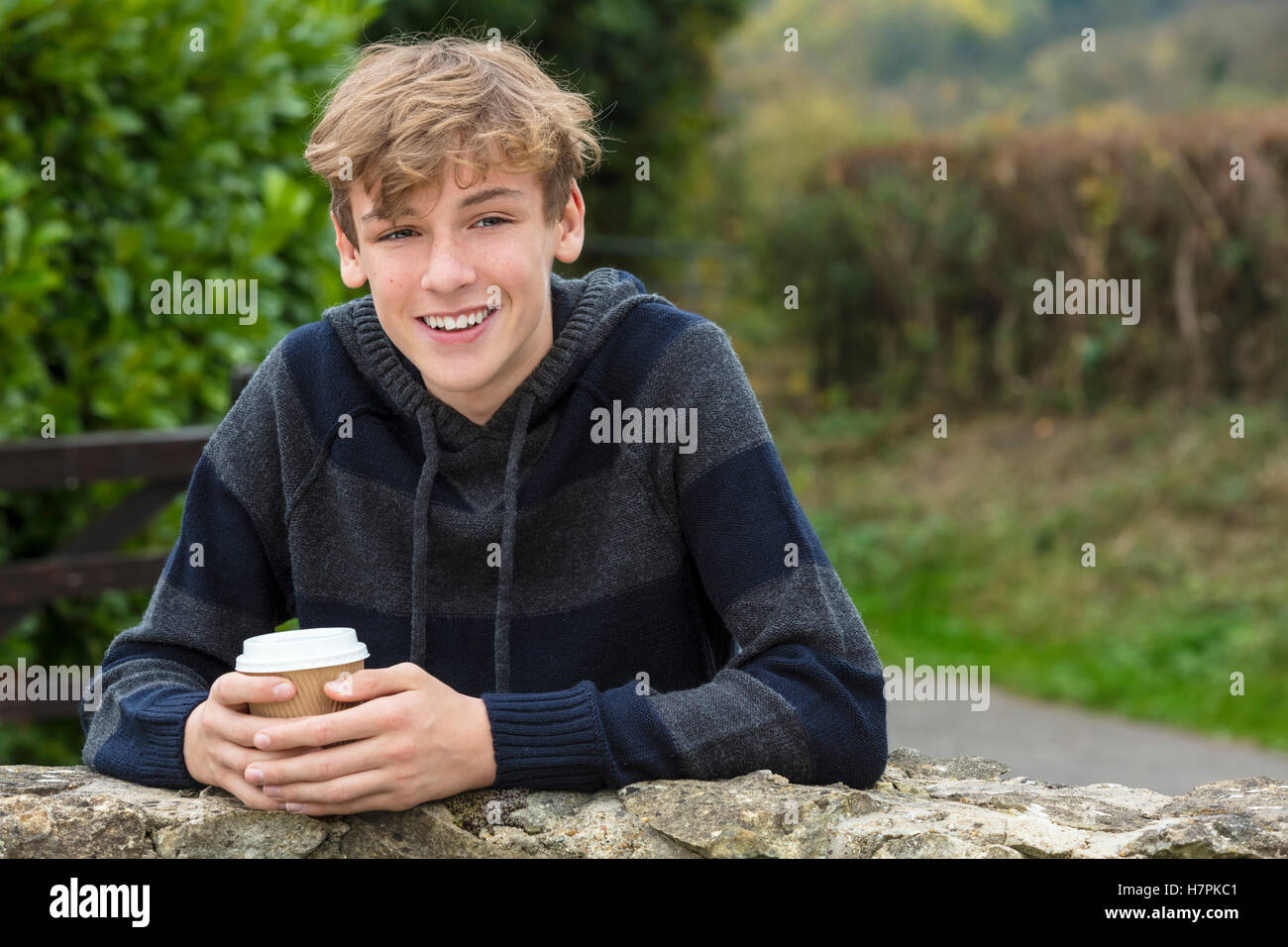 Young happy laughing male boy teenager blond child young adult drinking takeaway coffee outside in fall sunshine Stock Photo