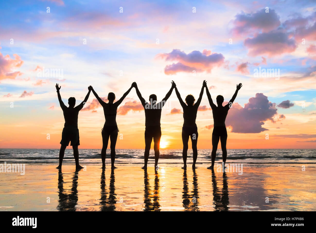 Silhouette of a group of people holding hands up on the beach with a beautiful sunset - concept about teamwork, friendship Stock Photo