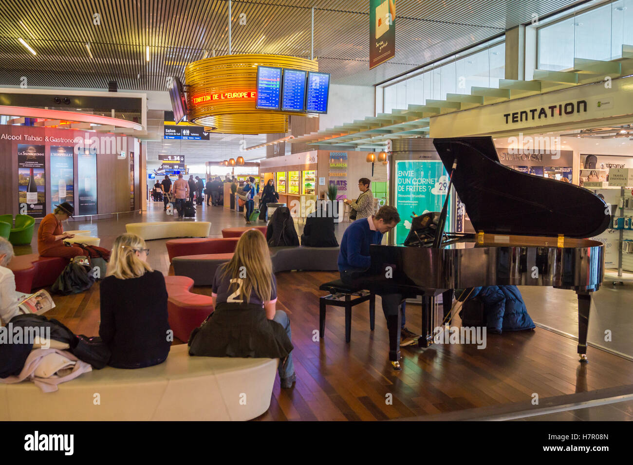 A passenger playing a public baby grand piano in the departures hall Toulouse airport, Blagnac, Haute-Garonne, Occitanie, France Stock Photo