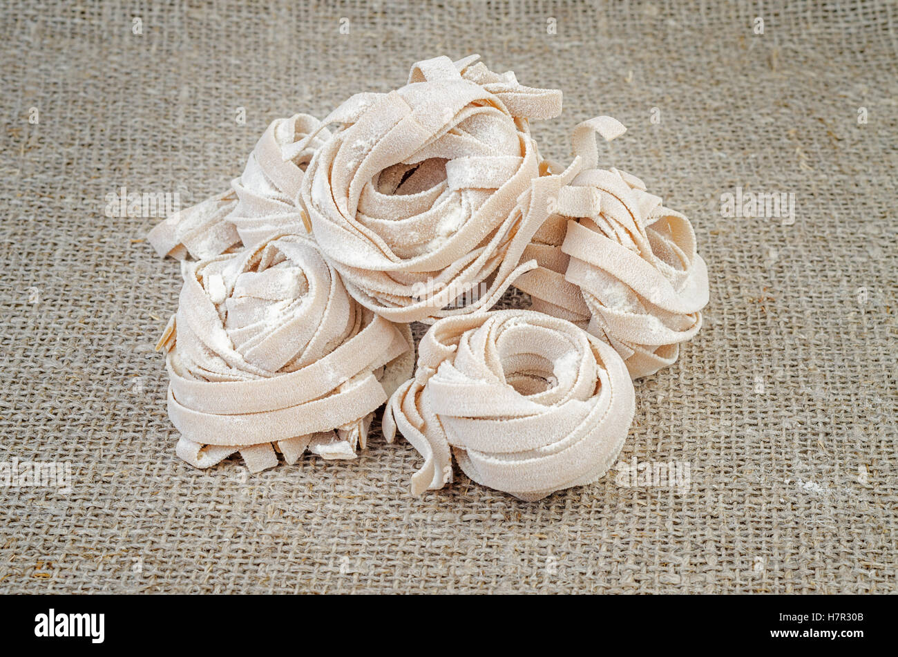 Uncooked homemade rolled traditional italian pasta on linen background. Portion of raw fettuccine or tagliatelle or pappardelle. Stock Photo