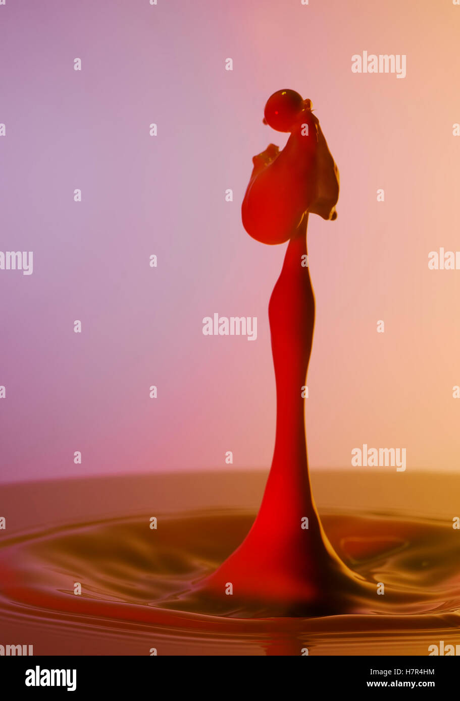 A red coloured water drop rising in the shape of a lady looking as ...