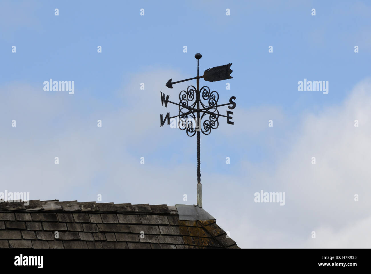 A wind vane on a shingled roof with the arrow pointing north
