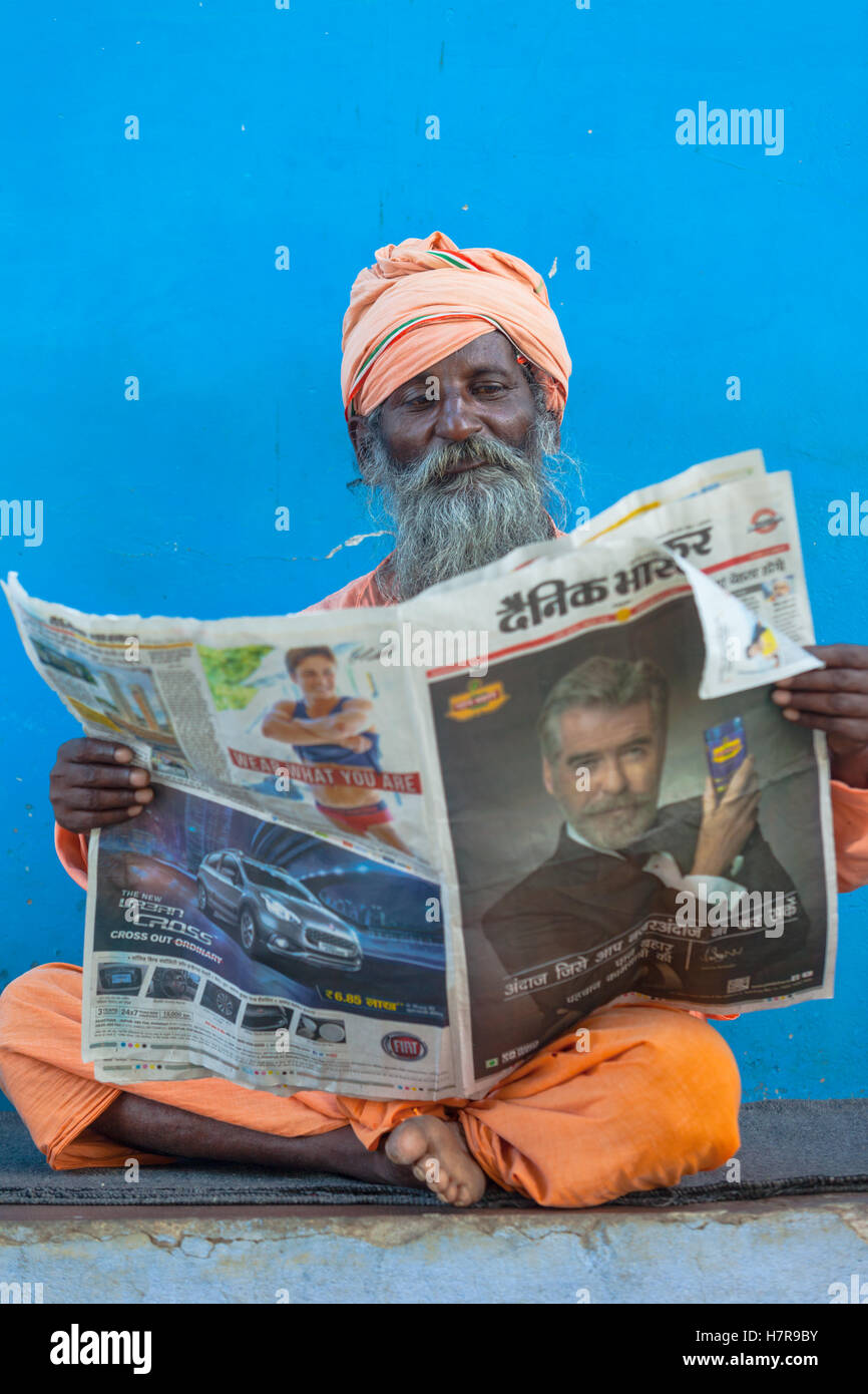 A Brahmin reading a newspaper against a blue wall, Pushkar, India Stock Photo