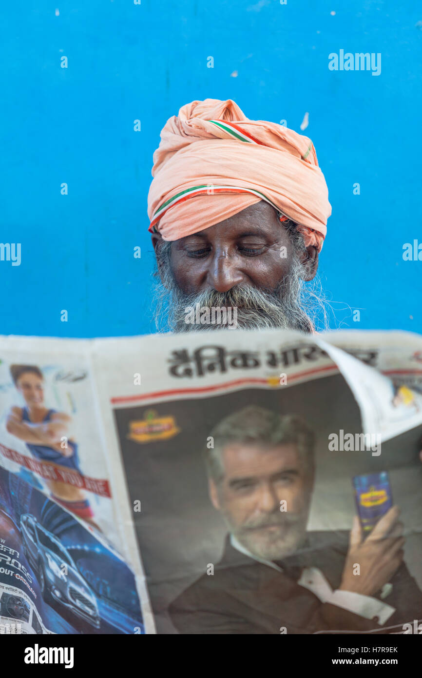 A Brahmin reading a newspaper against a blue wall, Pushkar, India Stock Photo