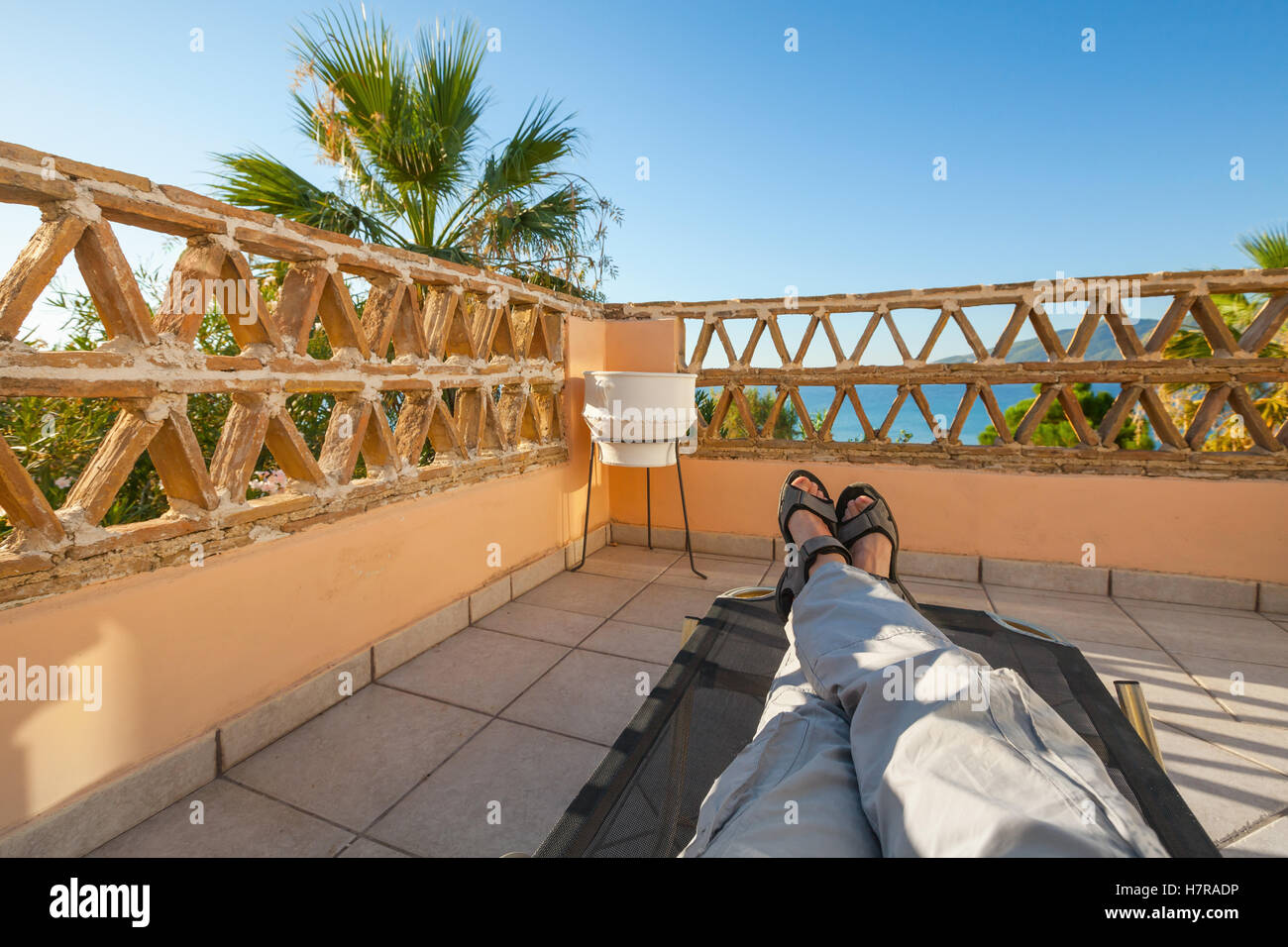 Feet of man relaxing on sun lounger, seaside balcony, popular touristic resort Zakynthos island, Greece Stock Photo