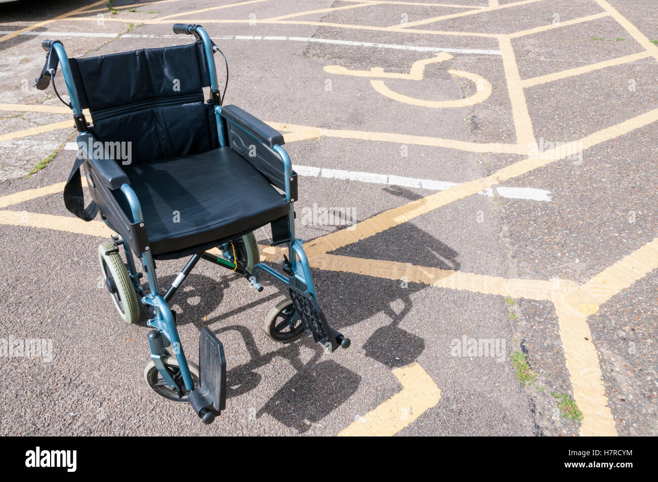 An empty wheelchair next to disabled parking bays in a car park. Stock Photo