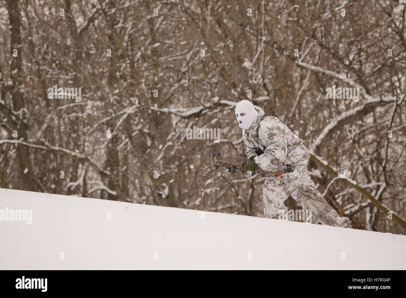 Male Bowhunter Draws Bow In Snow While Deer Hunting Stock Photo