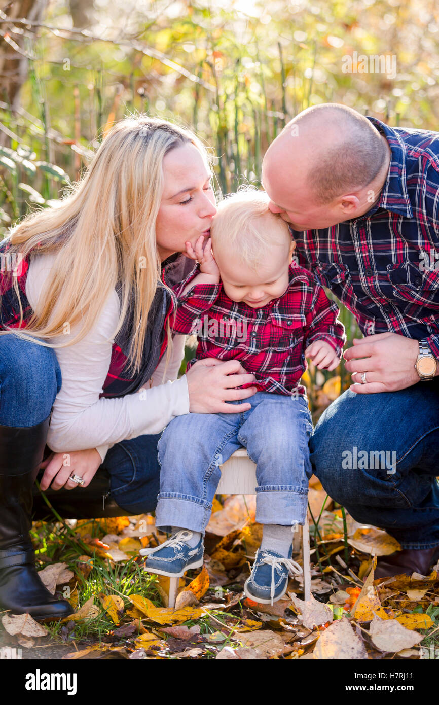 A young couple kisses their toddler son's head while he swirms away during family portraits in autumn; Surrey, British Columbia, Canada Stock Photo