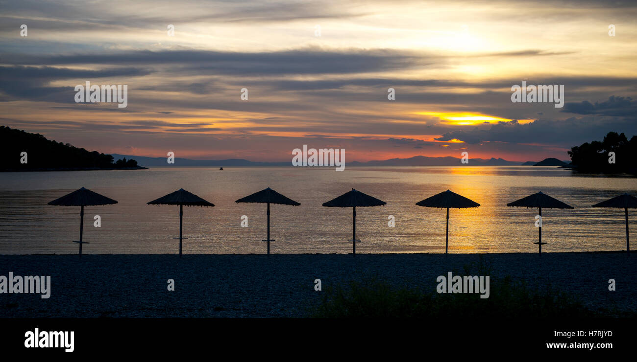 Silhouette of umbrellas on the beach at sunset on a greek island along the Aegean sea; Panormos, Thessalia Sterea Ellada, Greece Stock Photo