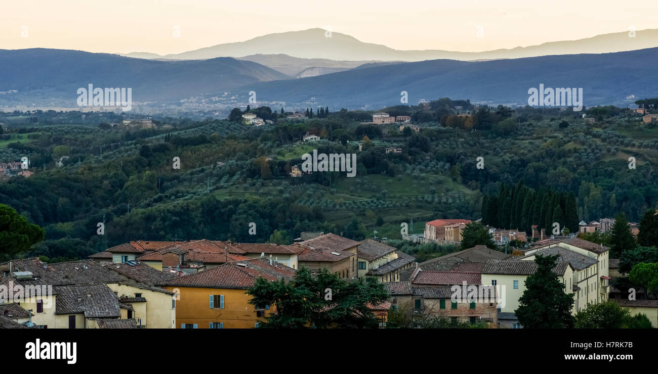 Silhouetted mountains in the distance at dusk and houses in the foreground; Siena, Italy Stock Photo