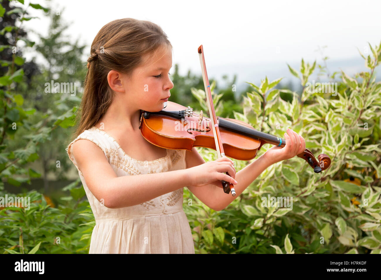 A young girl playing a violin in her yard; Salmon Arm, British Columbia, Canada Stock Photo