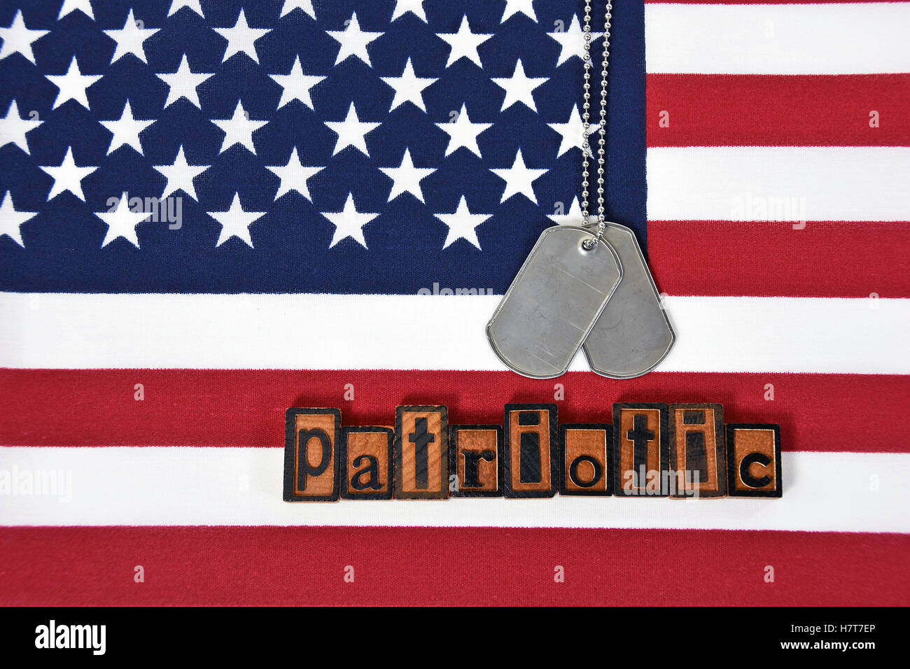 word patriotic in vintage wooden letterpress type with dog tags on American flag Stock Photo