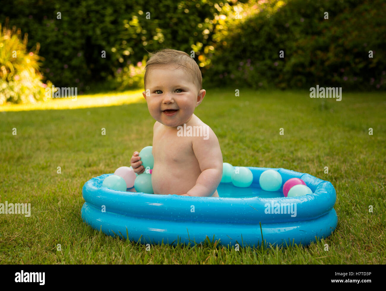 baby girl in a paddling pool in a garden during summer Stock Photo