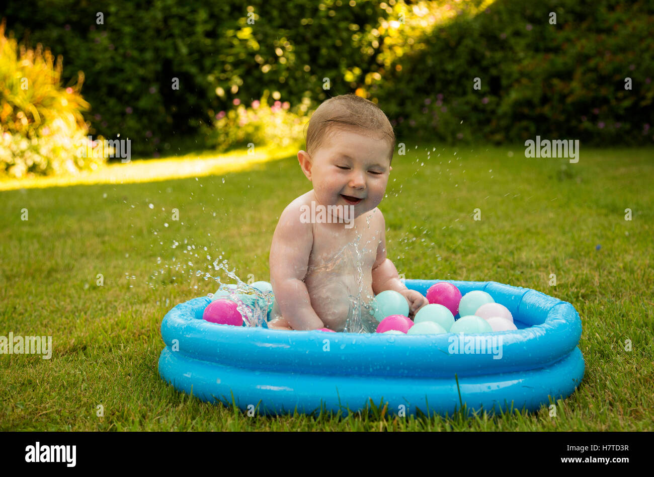 baby girl splashing in a paddling pool in summer Stock Photo