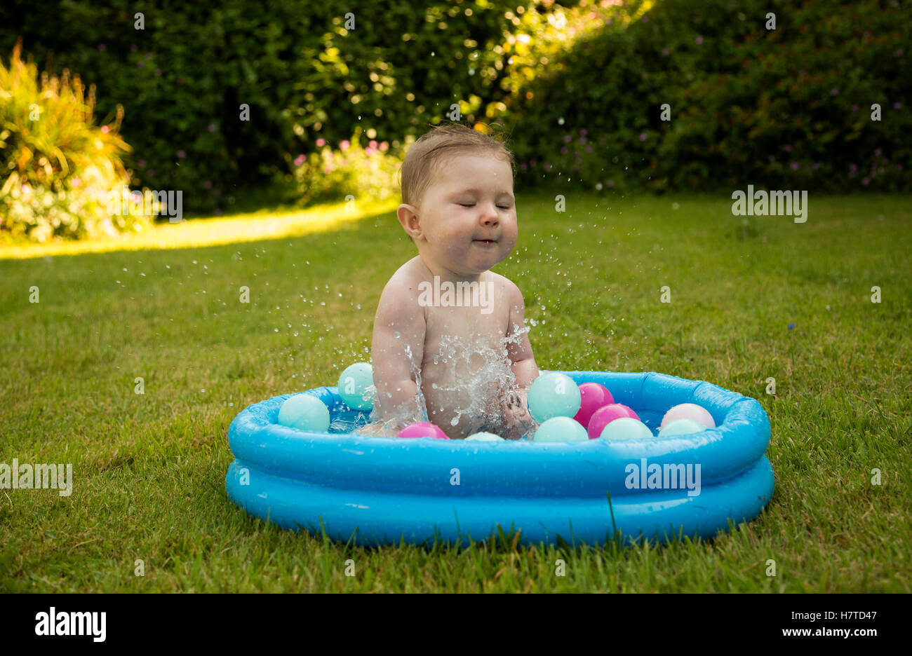 baby girl splashing in a paddling pool in summer Stock Photo