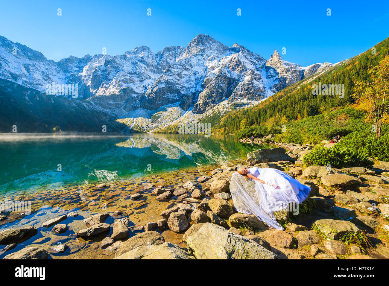 MORSKIE OKO LAKE, TATRA MOUNTAINS - SEP 24, 2016: young bride in white dress posing on rock during photo shoot at Morskie Oko la Stock Photo