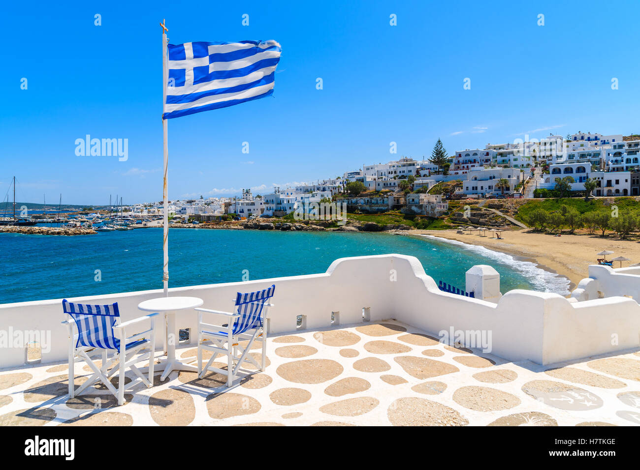 Chairs with table on a terrace with Greek flag in Naoussa village, Paros island, Greece Stock Photo