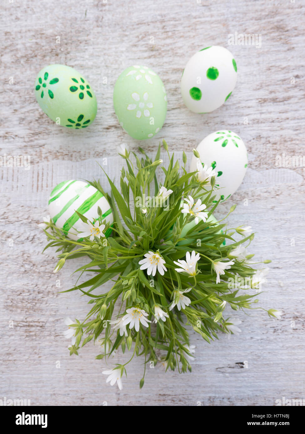 White and green easter eggs decorated by stripes, dots and flowers and wild flowers bouquet on the white wooden board Stock Photo