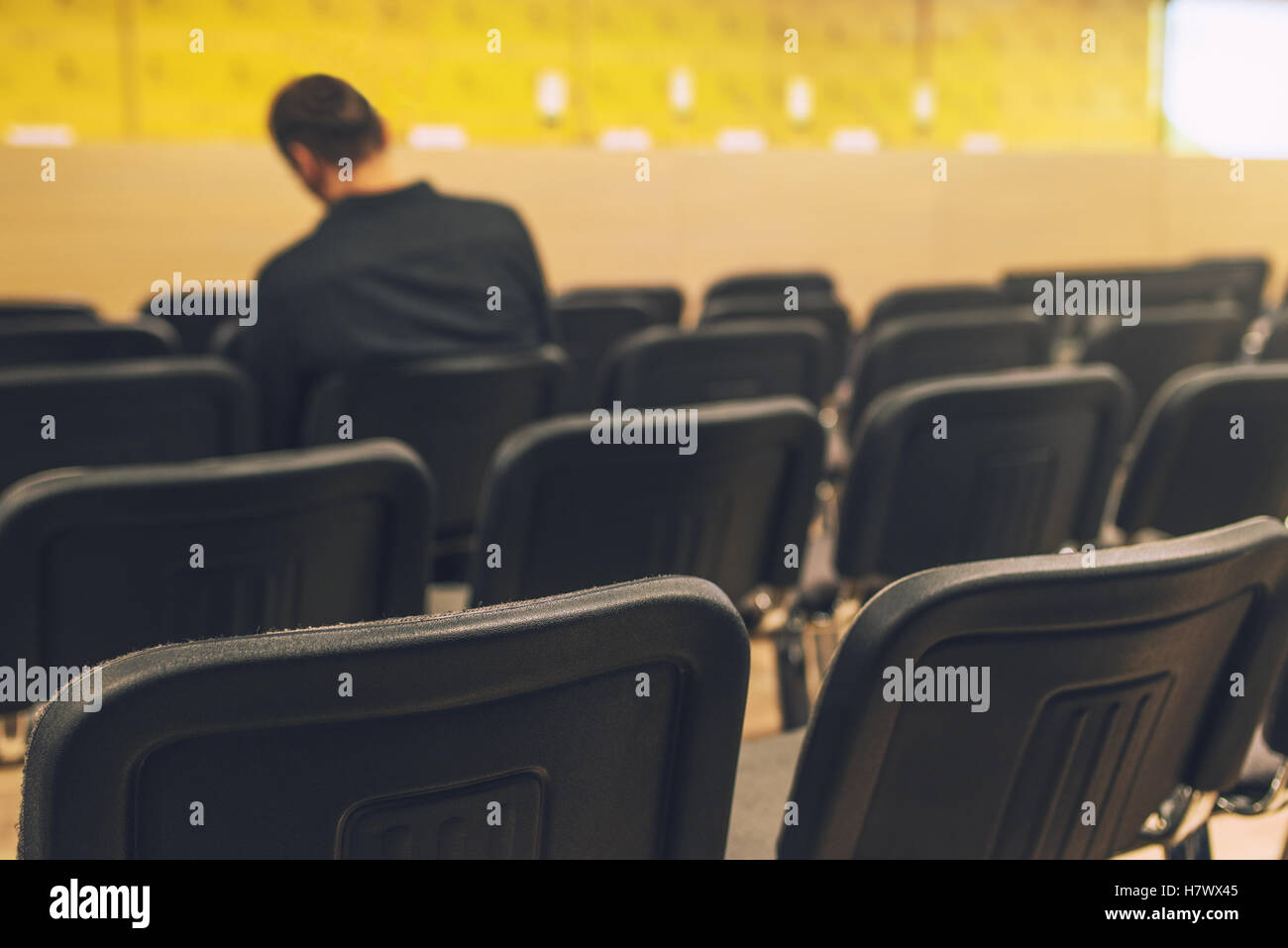 Unrecognizable journalist in press conference room, sitting alone among empty chairs, selective focus Stock Photo