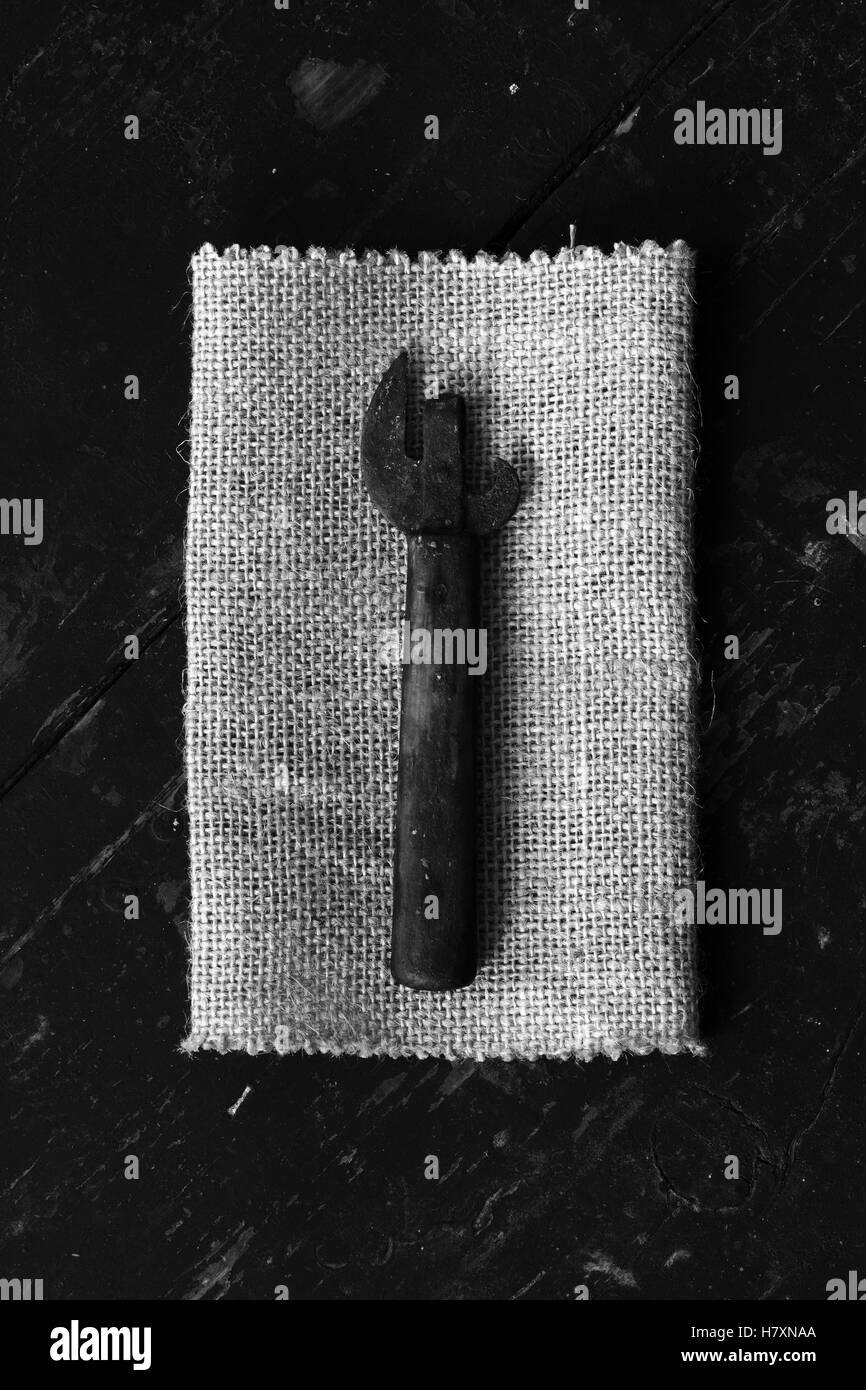 Old dirty can opener on the matting, on black boards. Top view closeup. Black and white photo. The concept of rustic kitchen Stock Photo