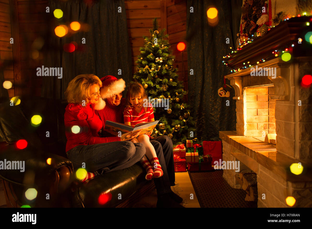 Family read book sitting on sofa in front of fireplace in Christmas decorated house interior Stock Photo