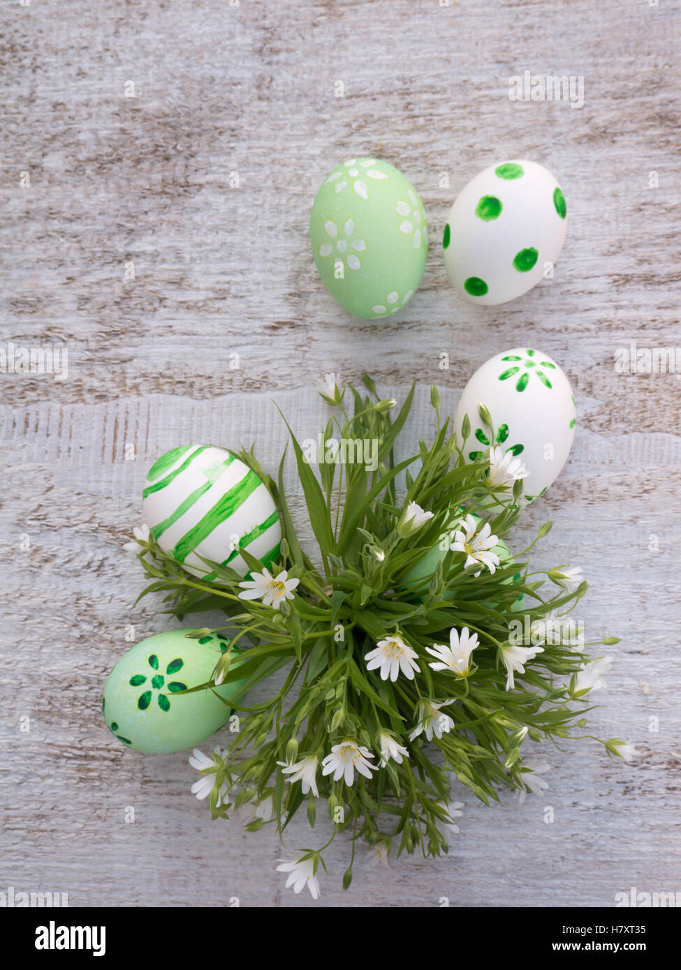 White and green easter eggs decorated by stripes, dots and flowers and wild flowers bouquet on the white wooden board Stock Photo