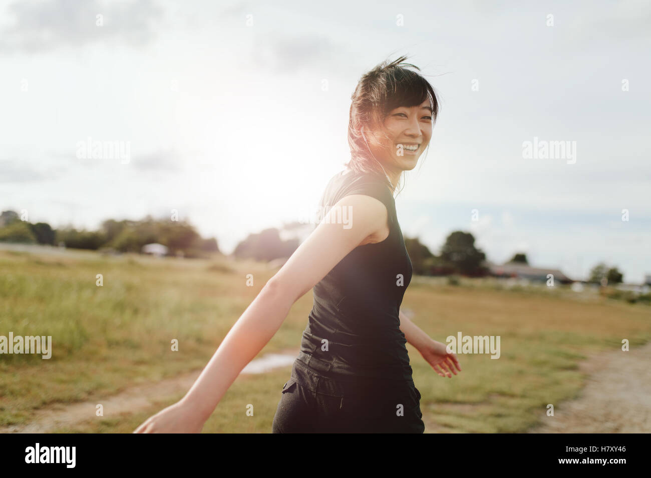Outdoor shot of smiling young woman runner looking at camera. Chinese female walking on field in morning. Stock Photo