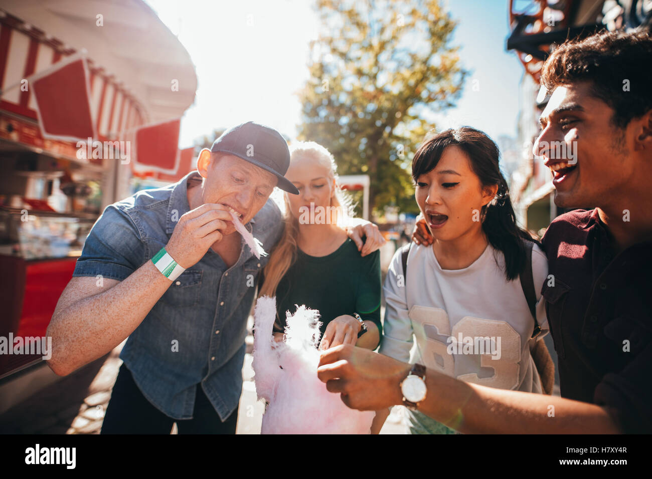 Group of friends eating cotton candy together in amusement park. Young man and women sharing cotton candyfloss at fairground. Stock Photo