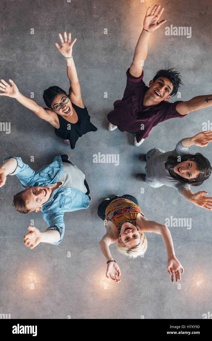 Overhead view of young people standing together looking up at camera with their arms raised. university students cheering. Stock Photo