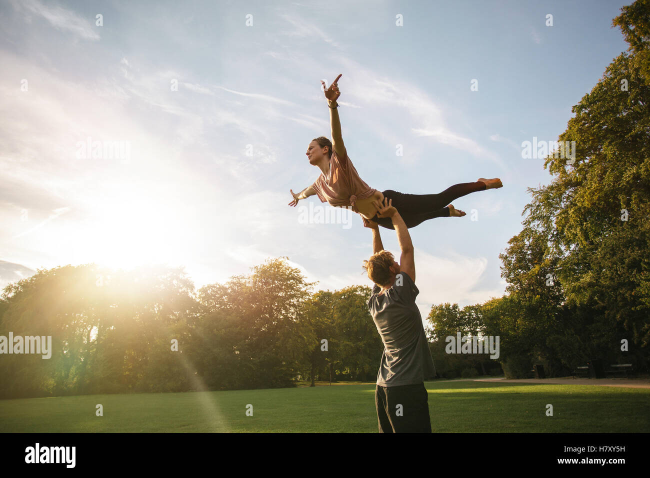 Strong young couple doing acroyoga outdoors. Man and woman in park practicing pair yoga. Stock Photo
