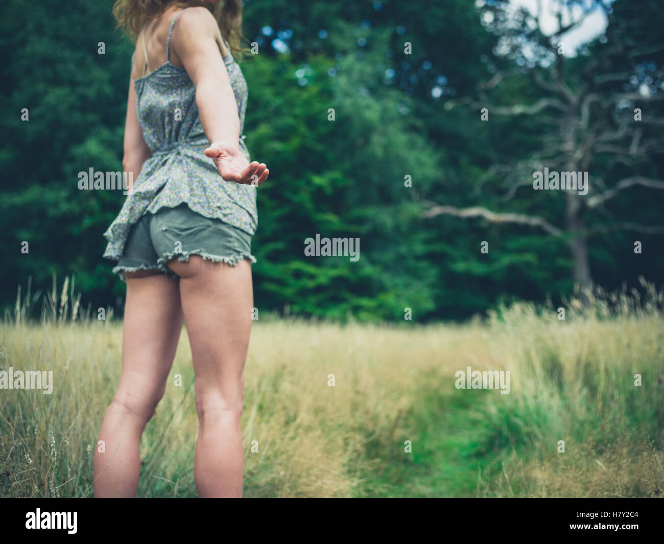 A young woman is standing in a meadow in the forest on a sunny summer day and is offering a helping hand Stock Photo