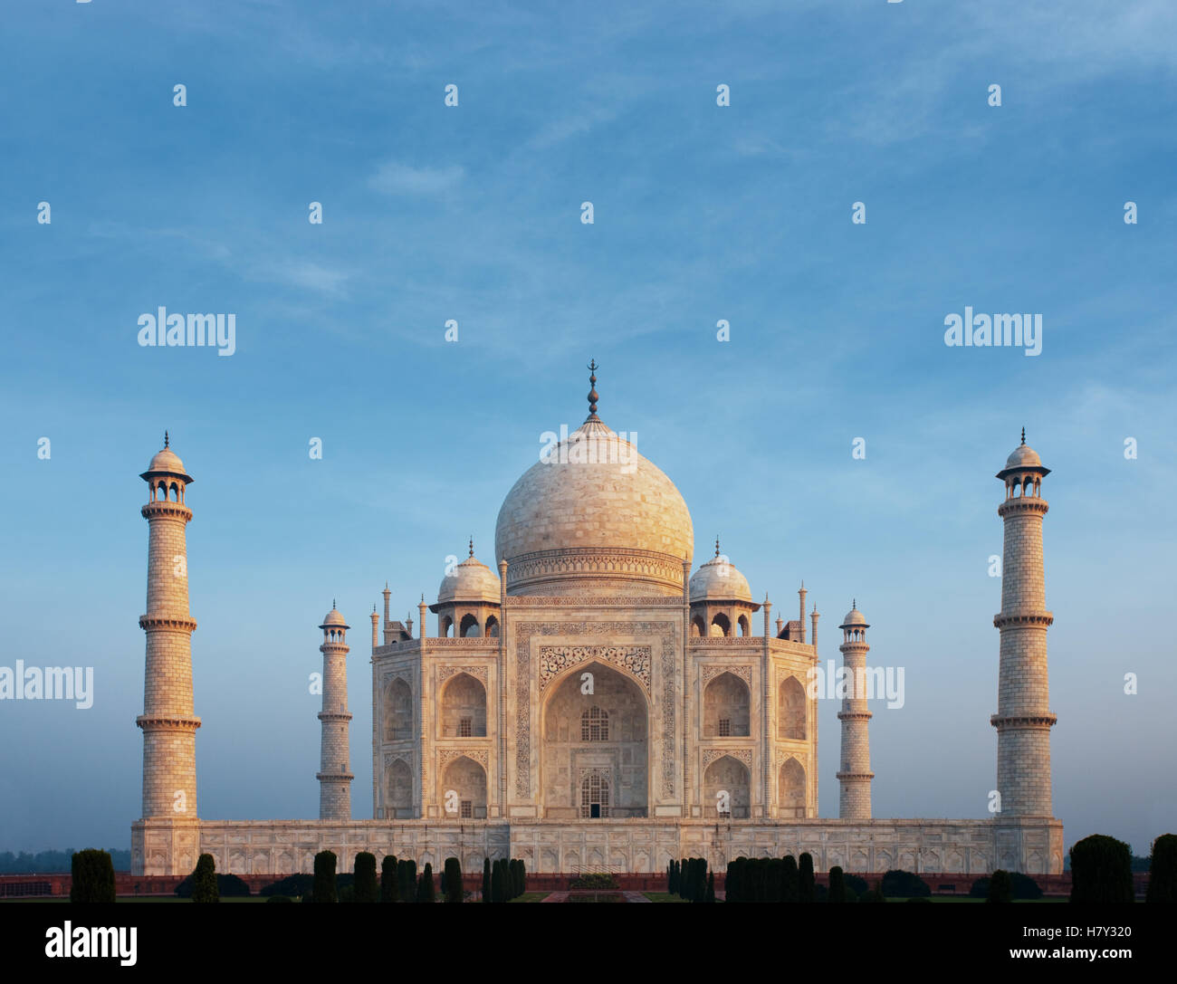A beautiful morning orange glow on front marble facade of the iconic Taj Mahal centered under a calm morning blue sky from telep Stock Photo