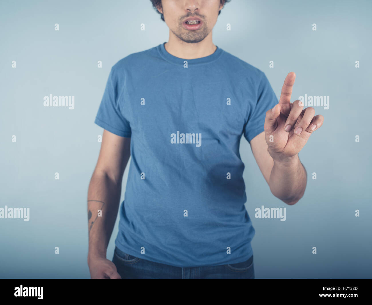 A young man wearing a blue t-shirt is raising his finger to either point or swipe or push Stock Photo