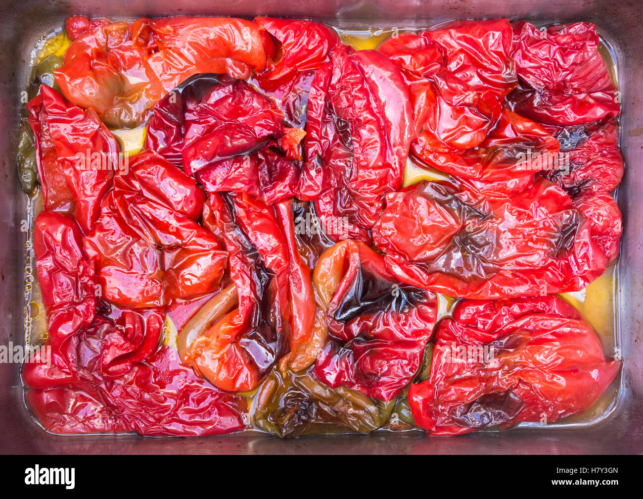 Overhead view of oven roasted red peppers in roasting tin with olive oil. Stock Photo