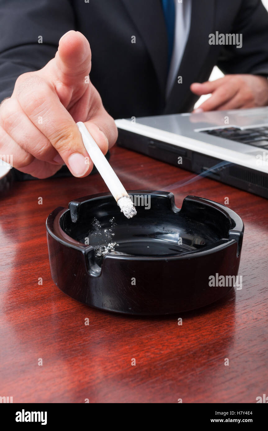 Close-up of ashtray with cigarette on office desk and business man at work  Stock Photo