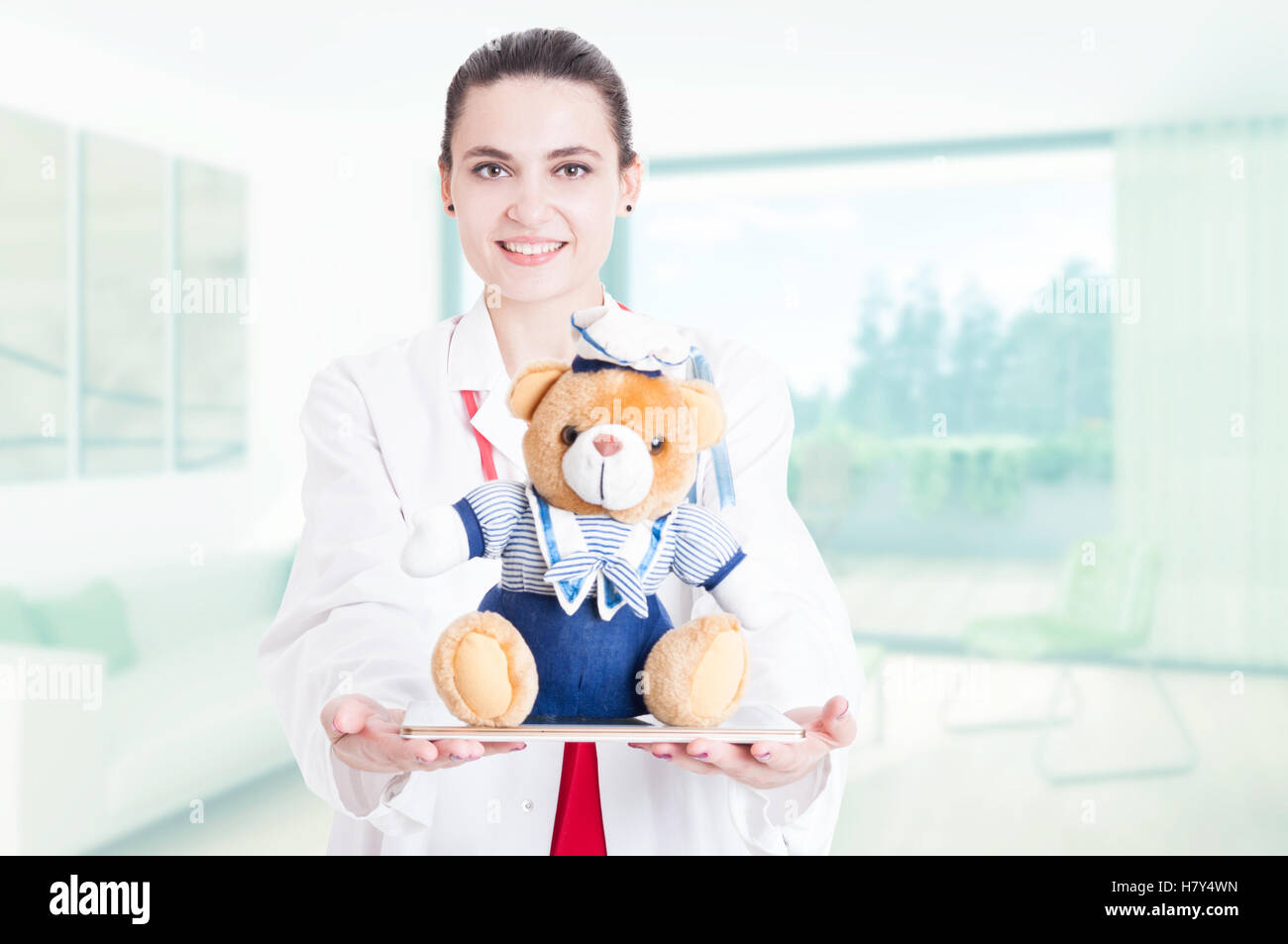 Beautiful and friendly pediatric doctor offering plush bear and tablet Stock Photo