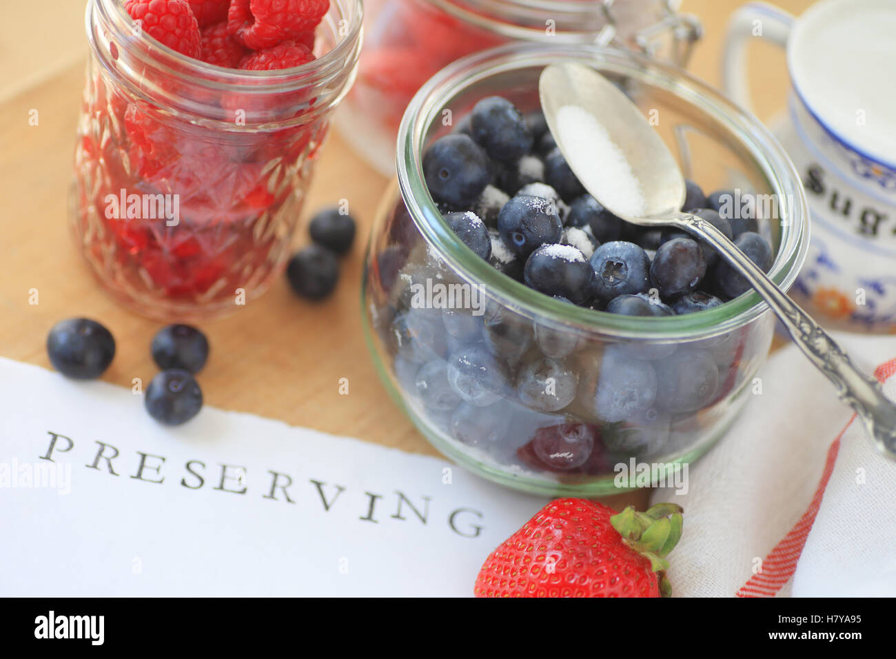 Blueberries, raspberries and strawberries in glass jars with sugar ready for making jam Stock Photo