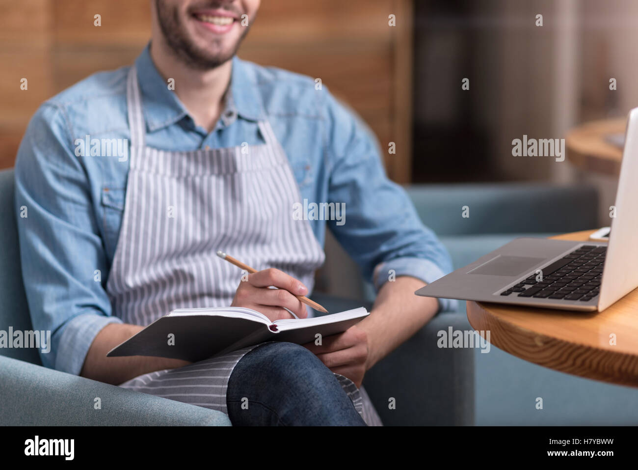 Smiling young man making notes and using laptop Stock Photo - Alamy