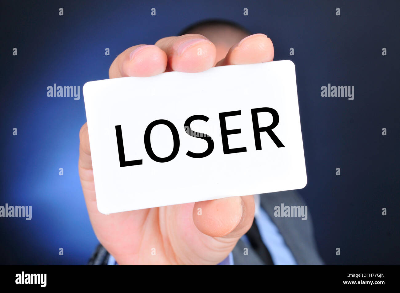 closeup of a young caucasian man in a gray suit showing a signboard with the word loser written in it Stock Photo